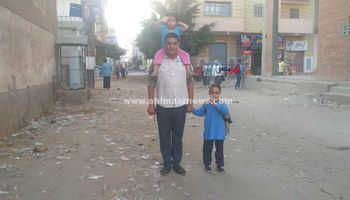 بنته الصغيرة على كتفه والتانية في إيده.. أب يوصل ابنته الصغيرة للمدرسة بأول أيام الدراسة بكفر الشيخ