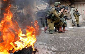 جندي إسرائيلي يصوب بندقيته على متظاهرين فلسطينيين في الخليل (رويترز)