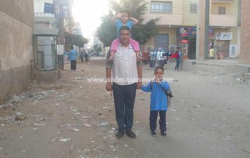 بنته الصغيرة على كتفه والتانية في إيده.. أب يوصل ابنته الصغيرة للمدرسة بأول أيام الدراسة بكفر الشيخ