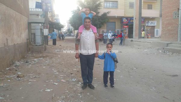 بنته الصغيرة على كتفه والتانية في إيده.. أب يوصل ابنته الصغيرة للمدرسة بأول أيام الدراسة بكفر الشيخ
