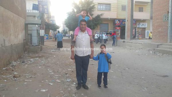 بنته الصغيرة على كتفه والتانية في إيده.. أب يوصل ابنته الصغيرة للمدرسة بأول أيام الدراسة بكفر الشيخ