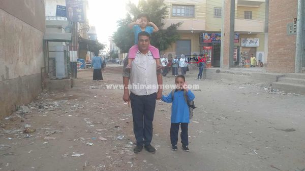 بنته الصغيرة على كتفه والتانية في إيده.. أب يوصل ابنته الصغيرة للمدرسة بأول أيام الدراسة بكفر الشيخ